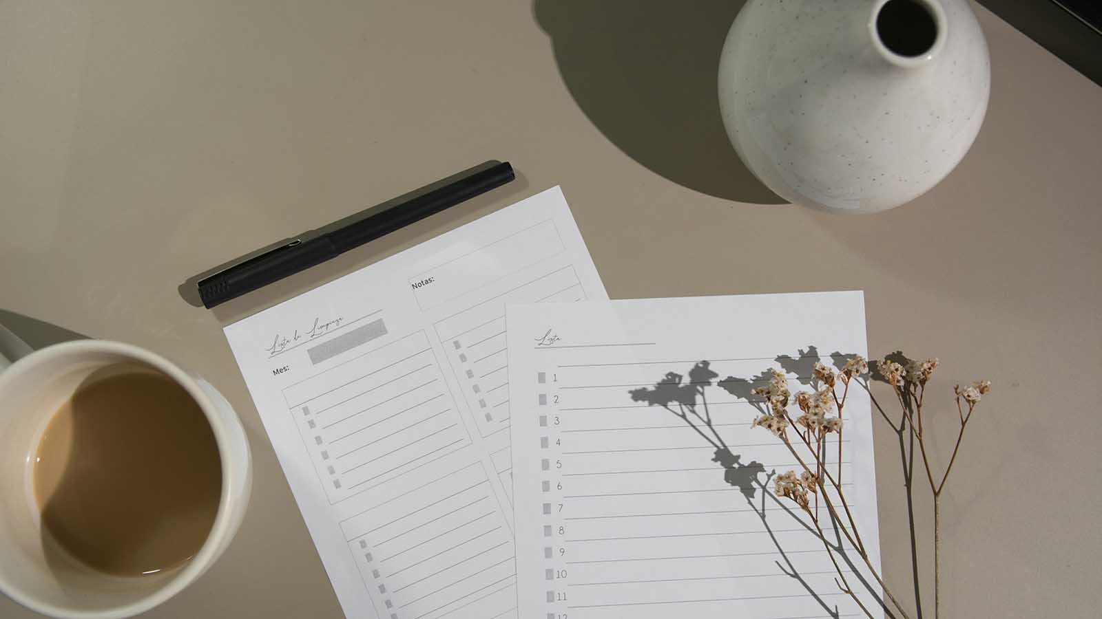 A couple of blank checklists on a table with a coffee, dried flowers, and a vase.