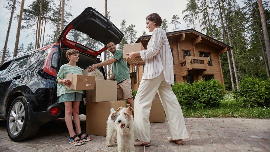 Full length portrait of happy family unloading boxes from car trunk while moving into new house with pet dog