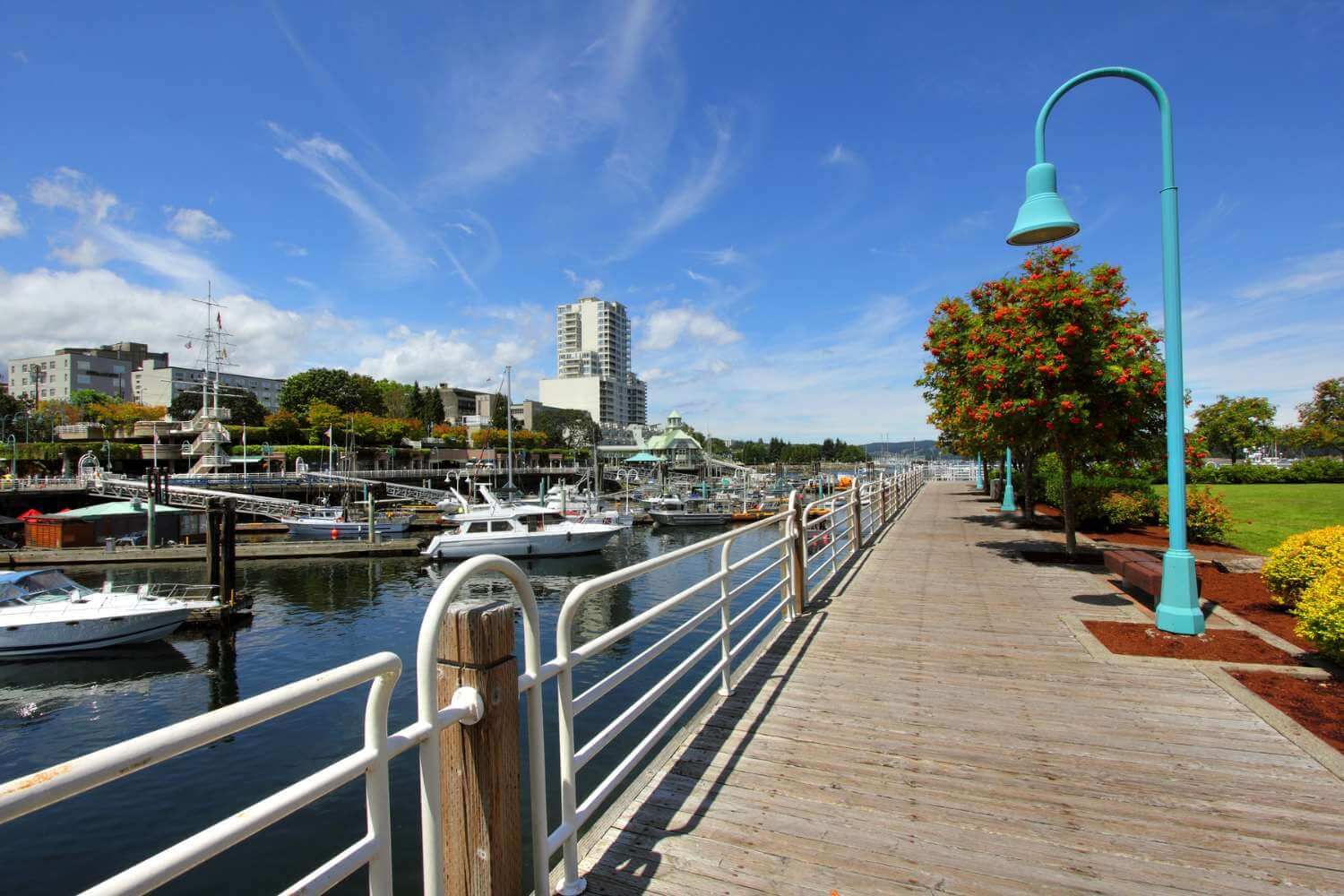 Nanaimo waterfront walkway with boats in the marina and street lamp and shrubs lining the walkway