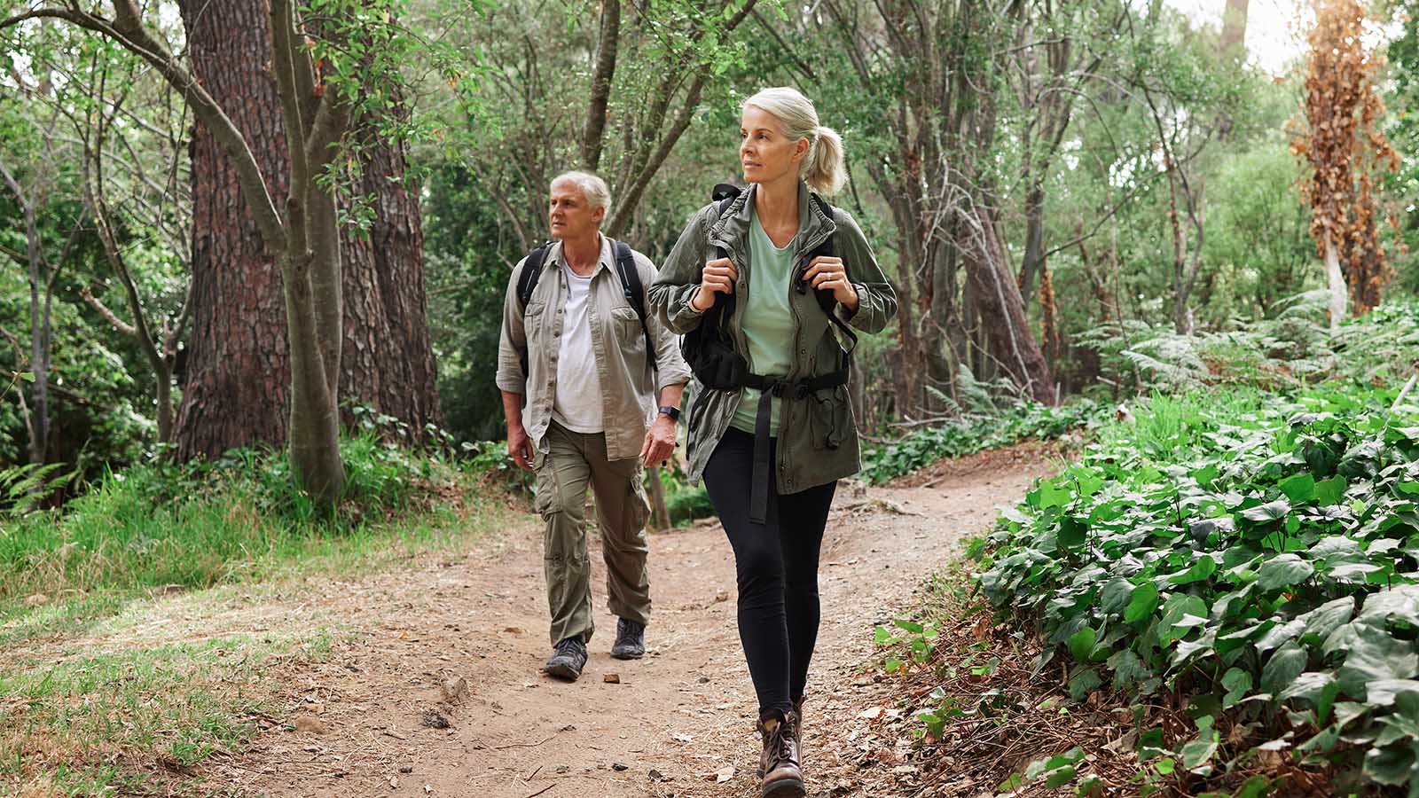 A mature caucasian couple out for a hike together. Senior man and woman smiling and walking in a forest in nature