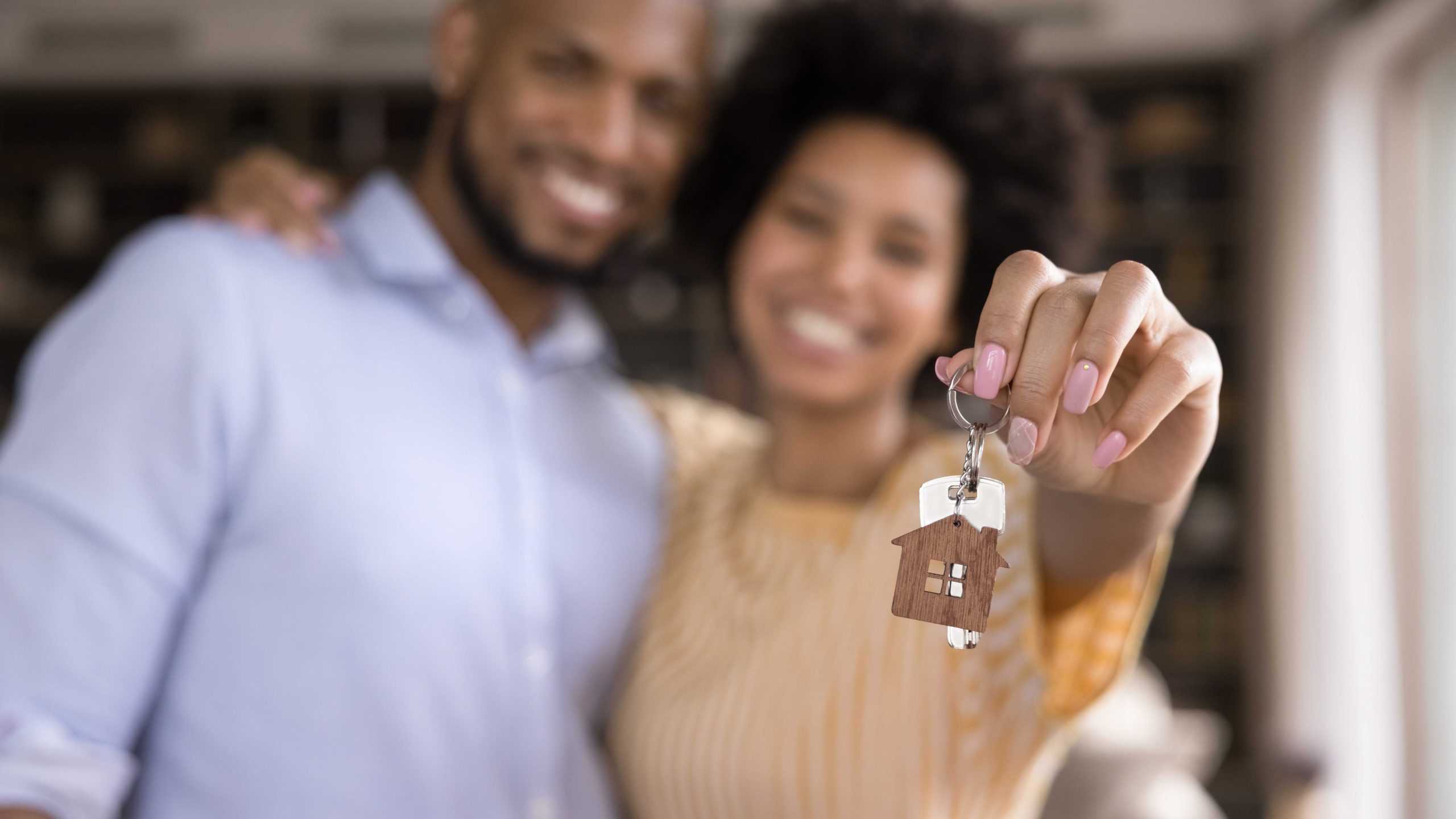 Close up focus on keys in hands of blurred joyful young loving african american married couple. Sincere mixed race homeowners celebrating purchasing own flat, feeling excited of renting new dwelling.