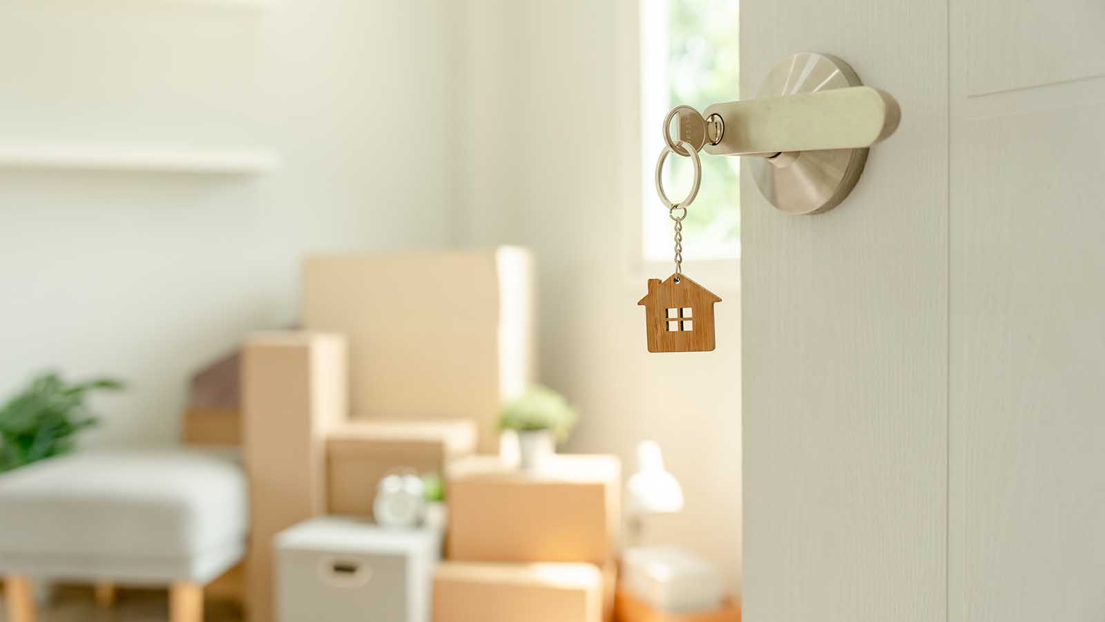 A key is inserted into the door of a new house, inside the room are cardboard boxes